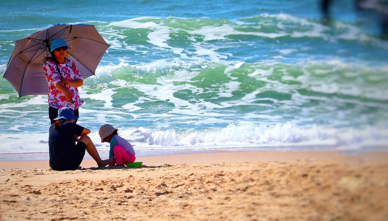 Family on the beach using an umbrella to protect from the sun. 