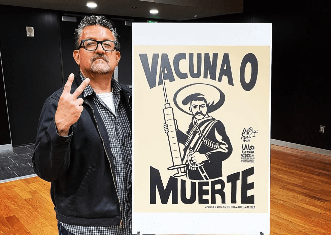 Lalo Alcaraz posing with a copy of his cartoon, Vacuna o Muerte(Vaccine or Death). Photo credit: Instagram/@laloalcaraz1