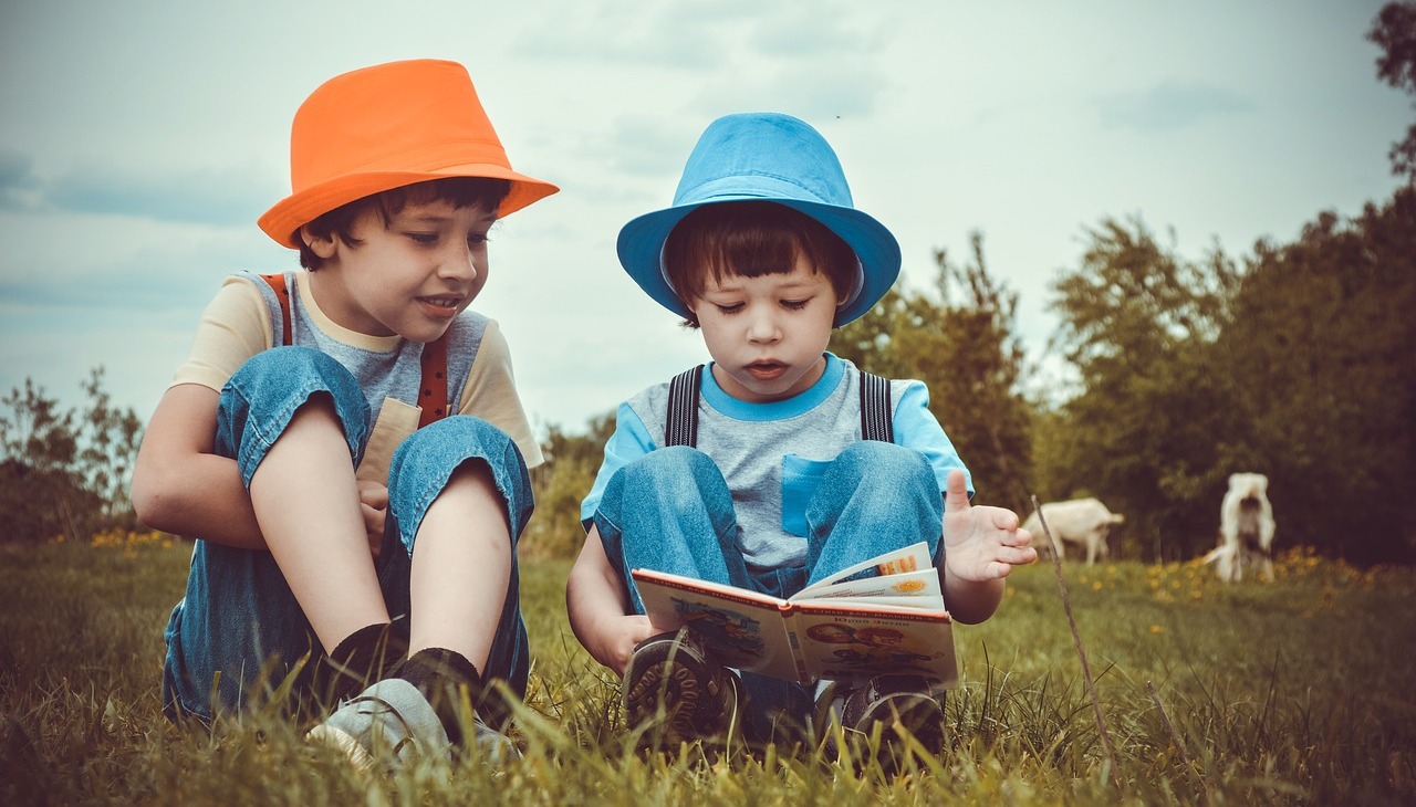 Kids reading a book sitting on the grass. 