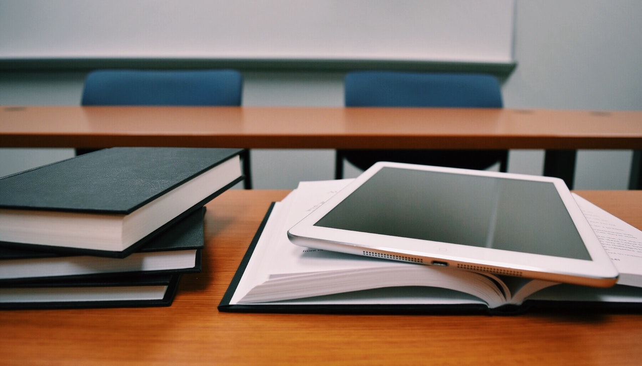 Books and a tablet on top of a classroom desk. 