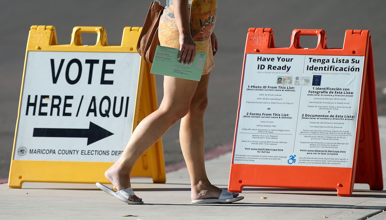 Pictured: Person walks to polling place. Signs that read Vote here/Aquí