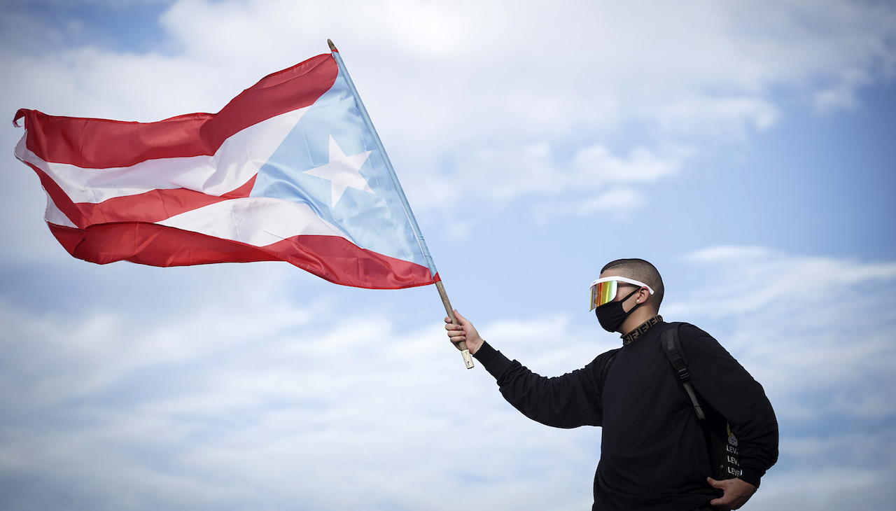 Pictured: Bad Bunny holds up Puerto Rican flag against blue sky