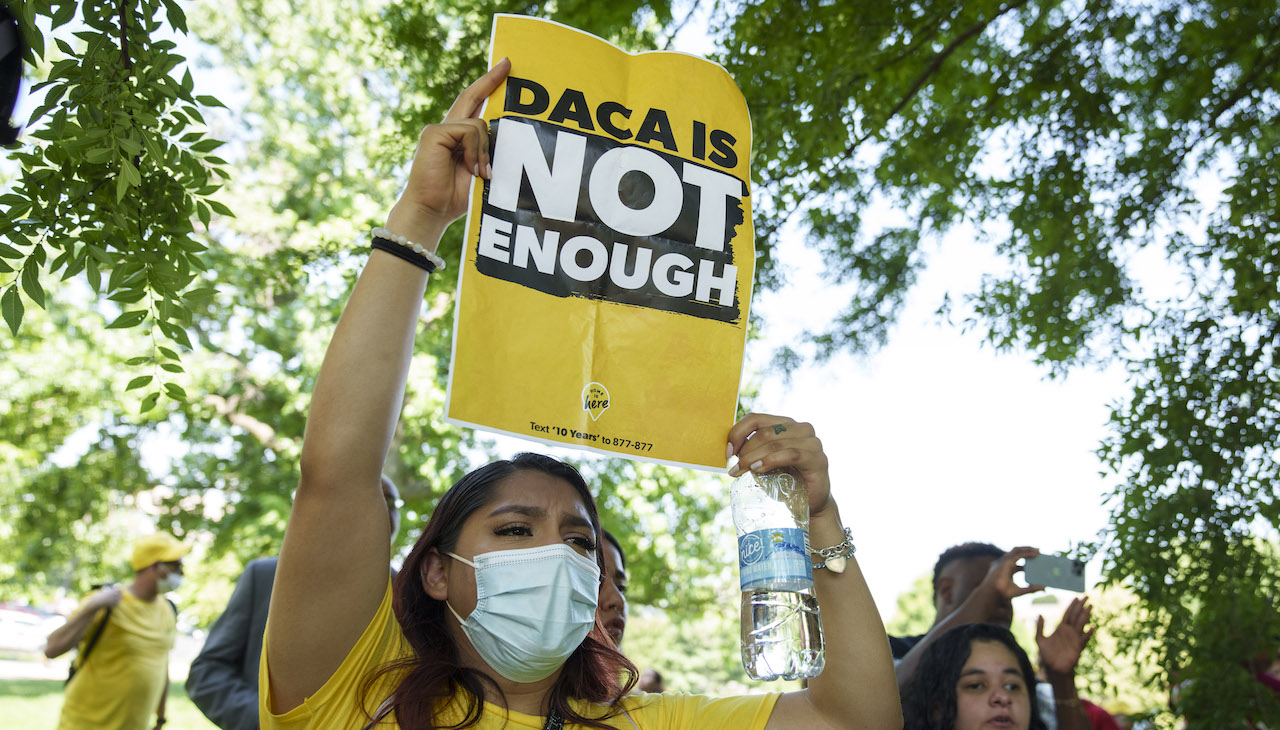 Pictured: Protesters march fo DACA holding a sign that reads, "DACA is not enough."