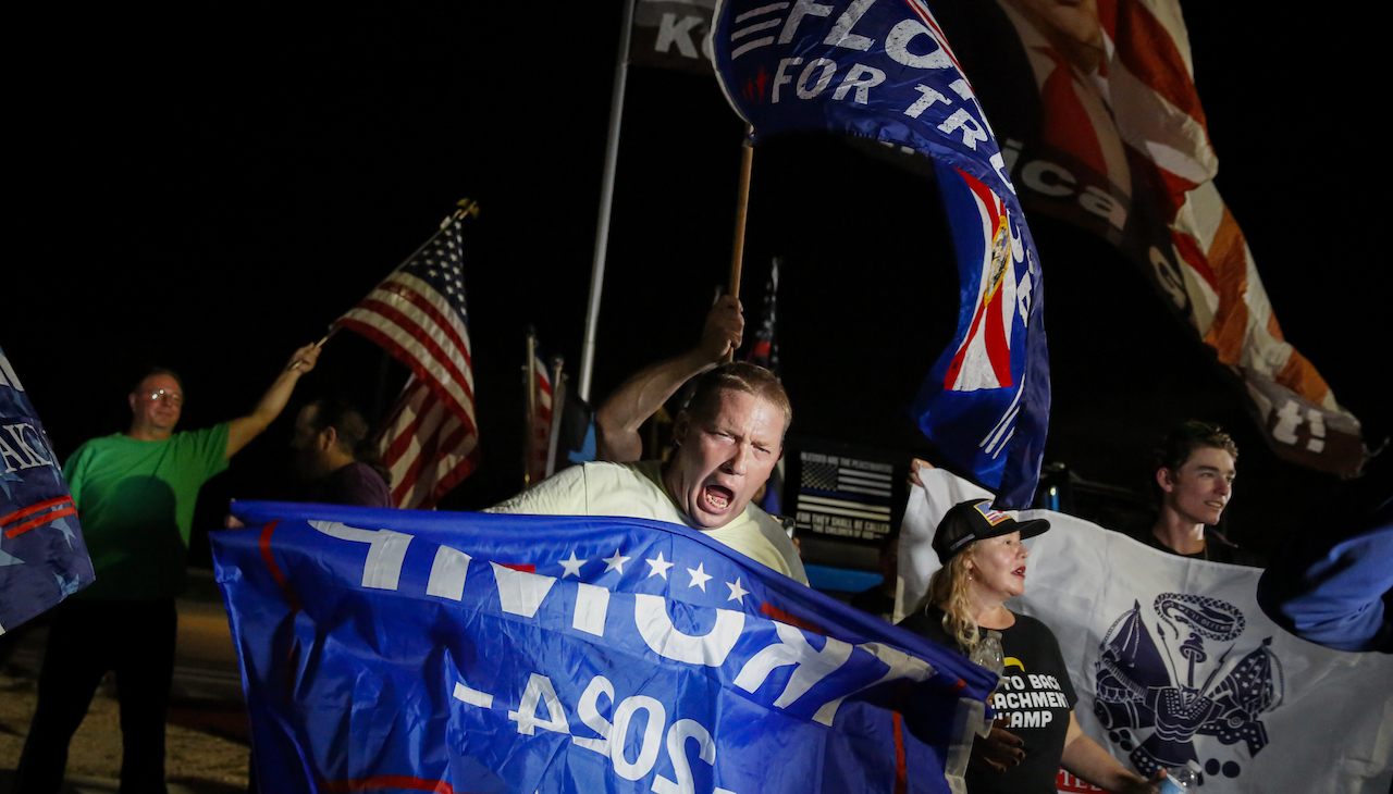 Pictured: Trump supporters holds Pictured: Trump flag in front of the former president's Mar-a-Lago resort.