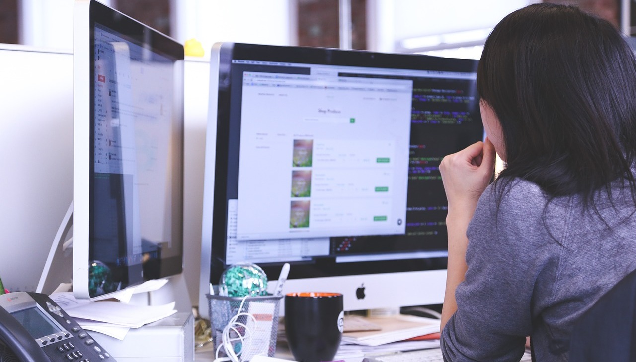 Woman working in front of two computer screens.