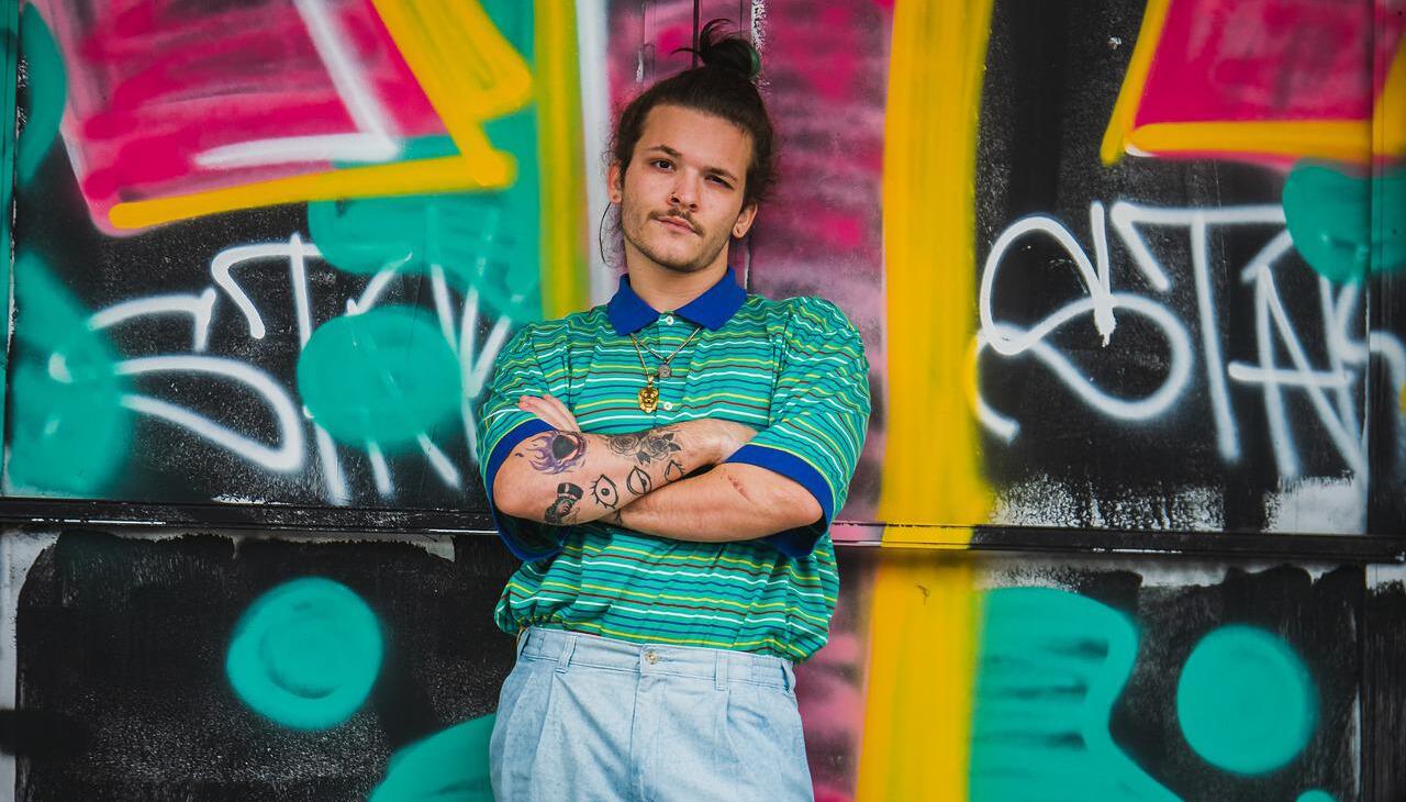 Latino man posing against a painted wall. 