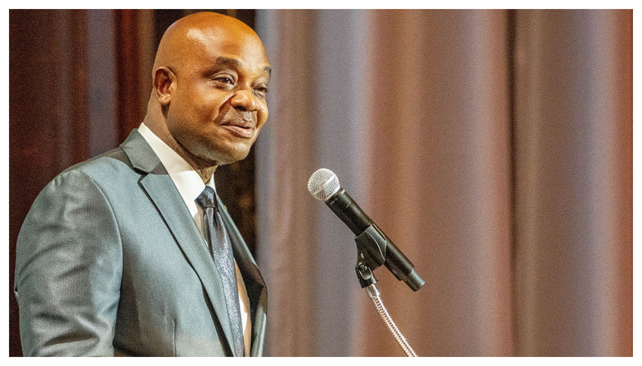 Luis Gilberto Murillo speaks into a microphone on a podium. He is a bald Afro-Latino man with dark skin wearing a gray suit. He is facing the right speaking to an audience out of view.