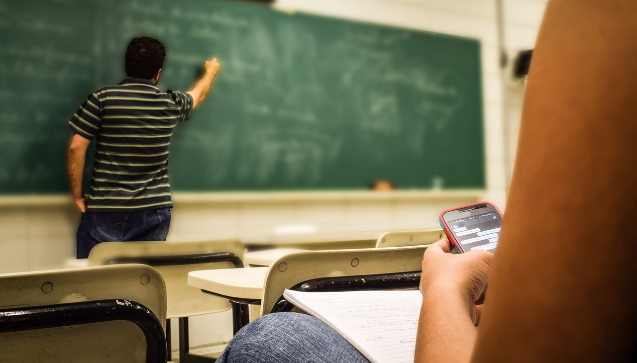 Teacher giving a class while student checks her phone. 