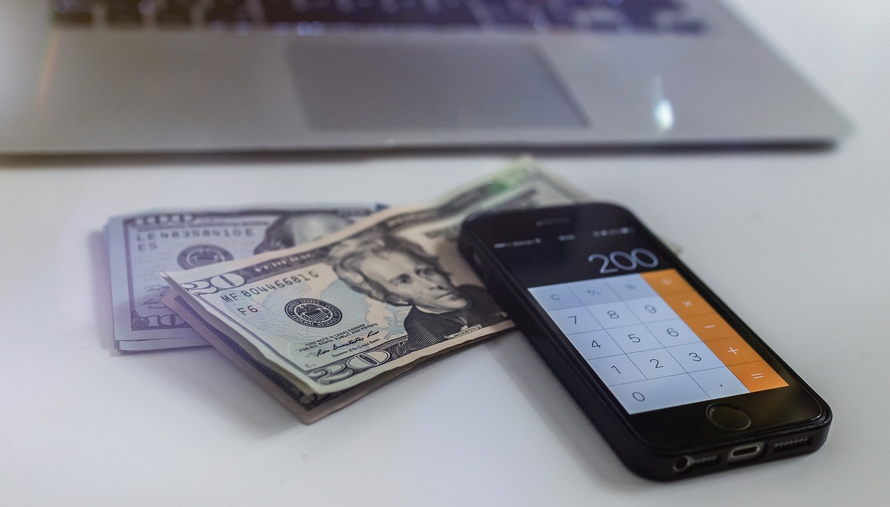 A calculator, some cash and a laptop on top of a table to illustrate financial education.