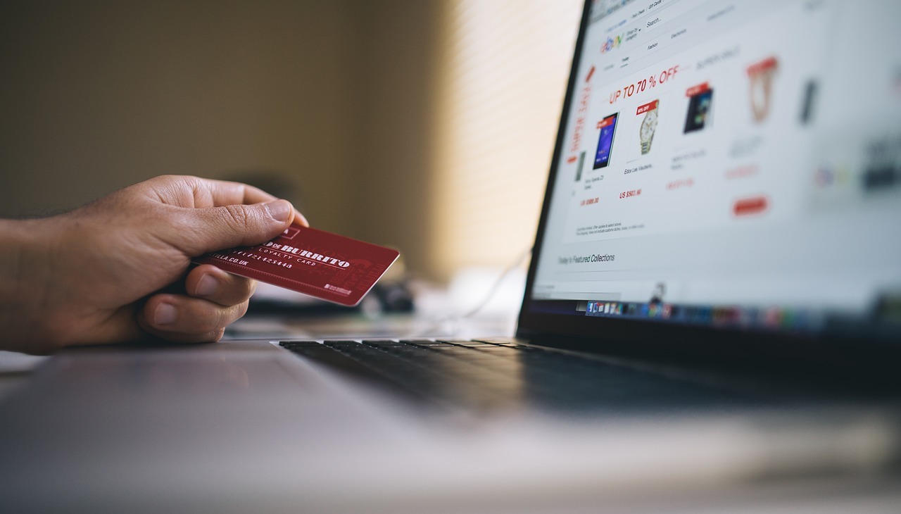 Hand holding a credit card in front of a laptop. 