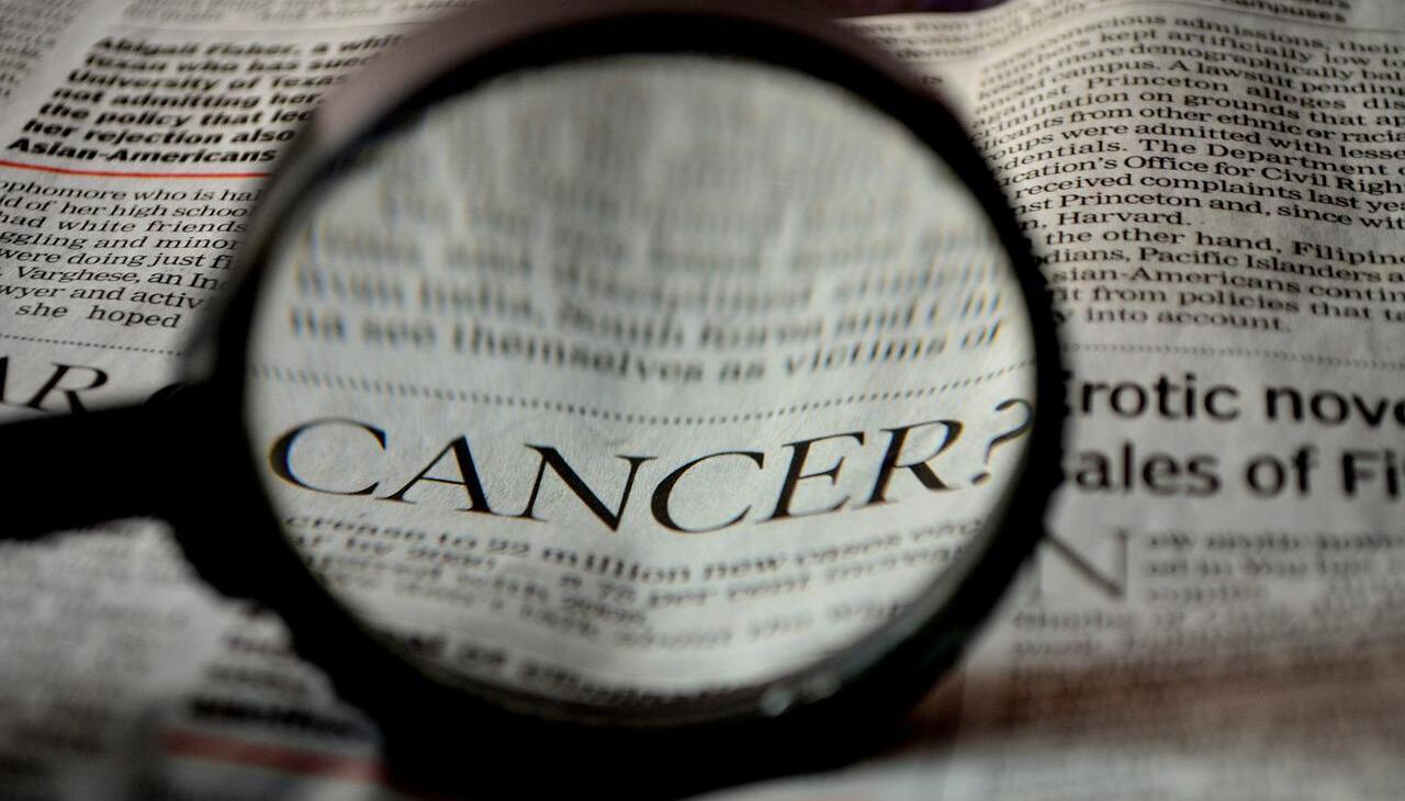 Magnifying glass showing the word cancer on a newspaper. 