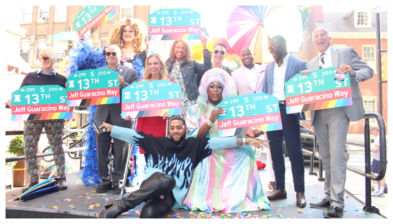 A group of people holding street signs. Each one reads "13th Street" with the text "Jeff Guaracino Way" highlighted in dark red beneath it.