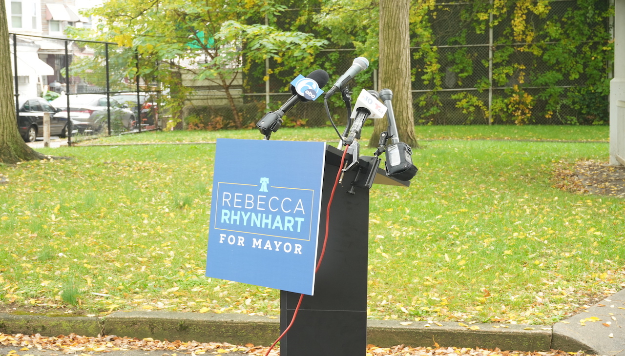 Pictured: Podium in West Philadelphia park with a sign that reads: Rebecca Rhynhart for Mayor