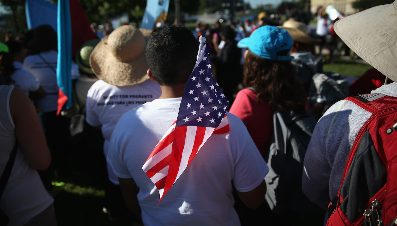 Pictured: Man stands amid a crowd holding American flag on his shoulder. Photo: John Moore/Getty Images.