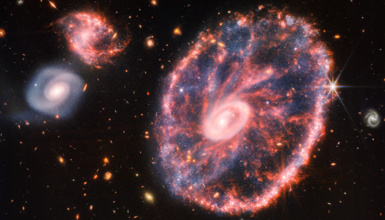 Mottled pink galaxy that looks like a wheel with a small inner oval. Photo: NASA