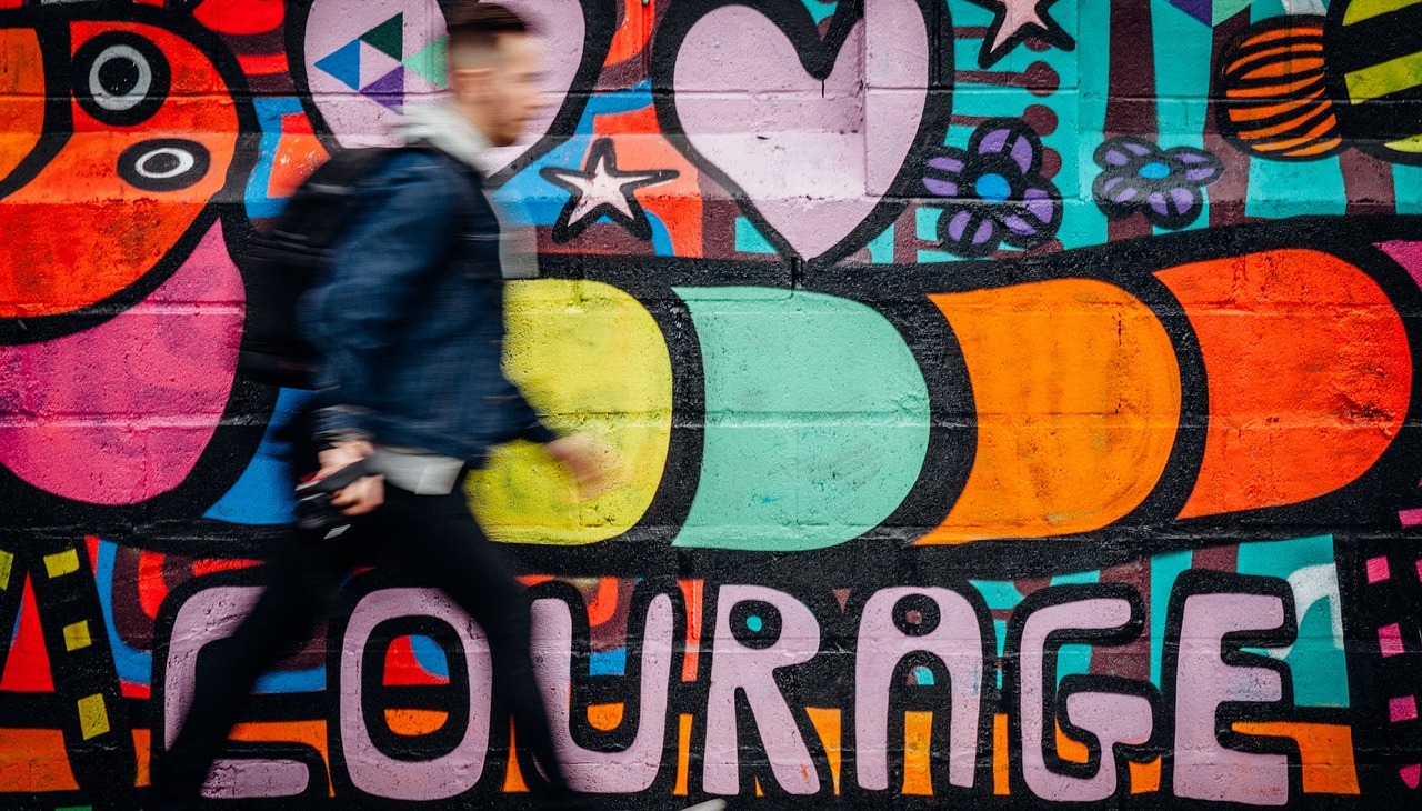 Young man walks next to a painted wall. 