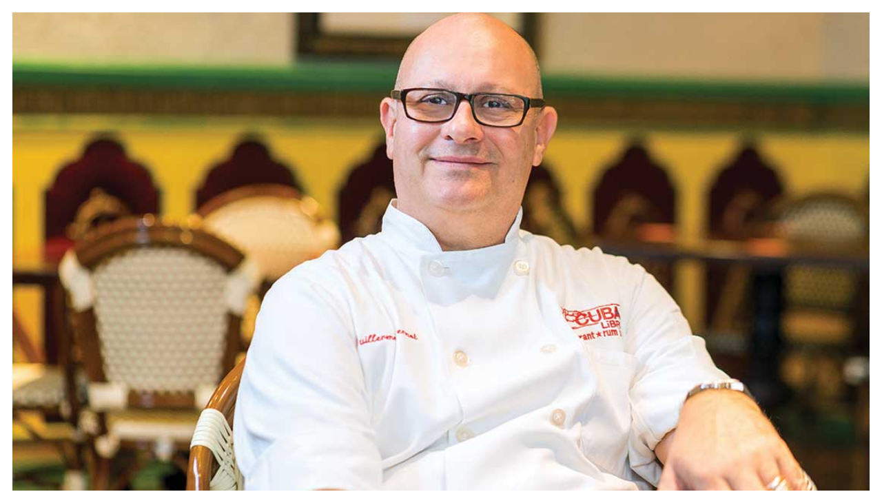 Guillermo Pernot, a bald man with glasses, wearing a white shirt. He is facing the viewer.