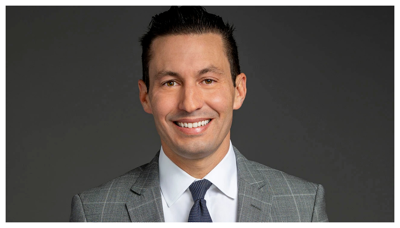 Dax Tejera, wearing a suir and tie. He is looking at the viewer and is smiling.