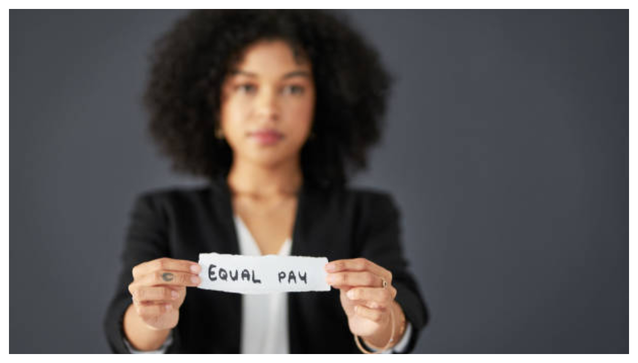 A woman holding a piece of paper reading "Equal Pay" with both hands.