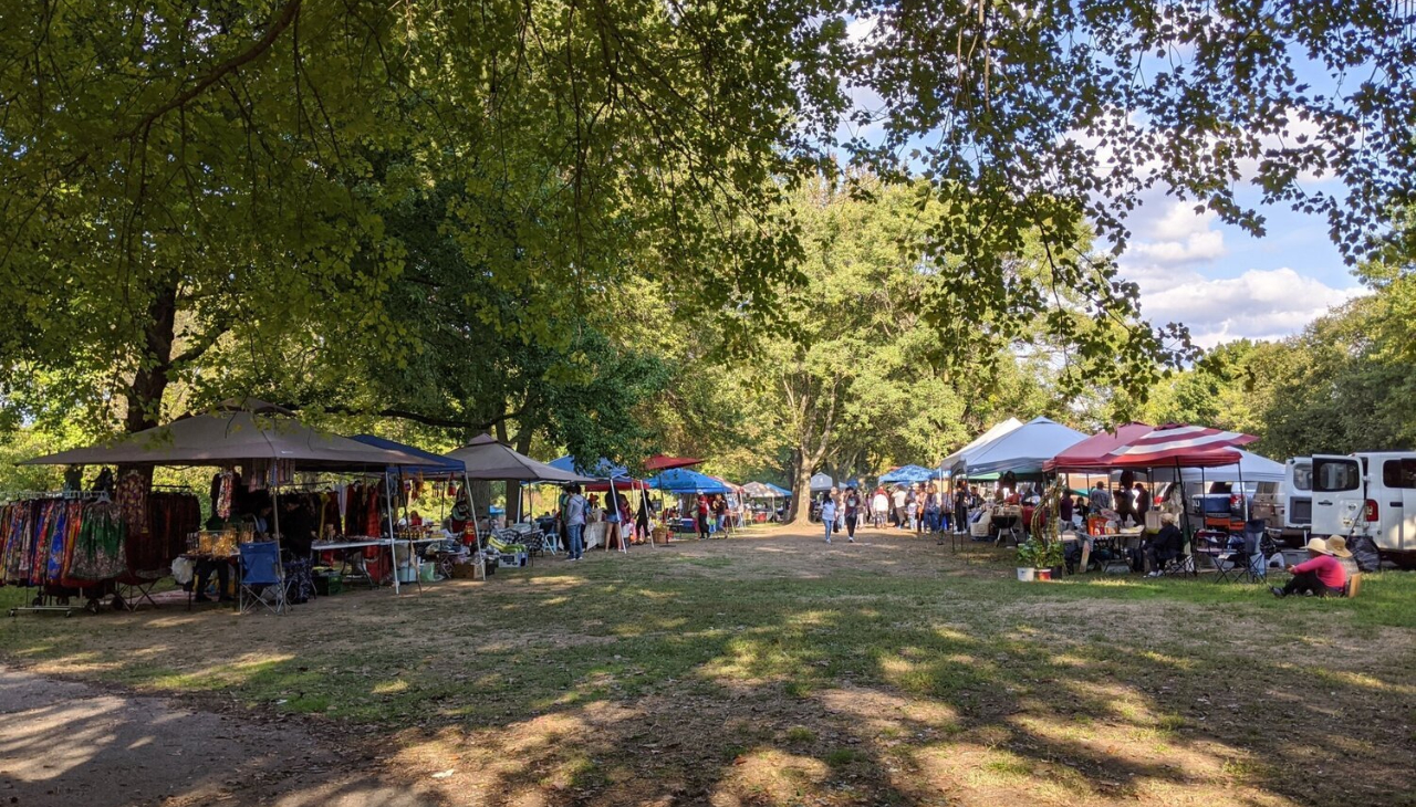 A field in FDR Park during the day. Multiple shops have set up along the edges of the clearing under portable tents.