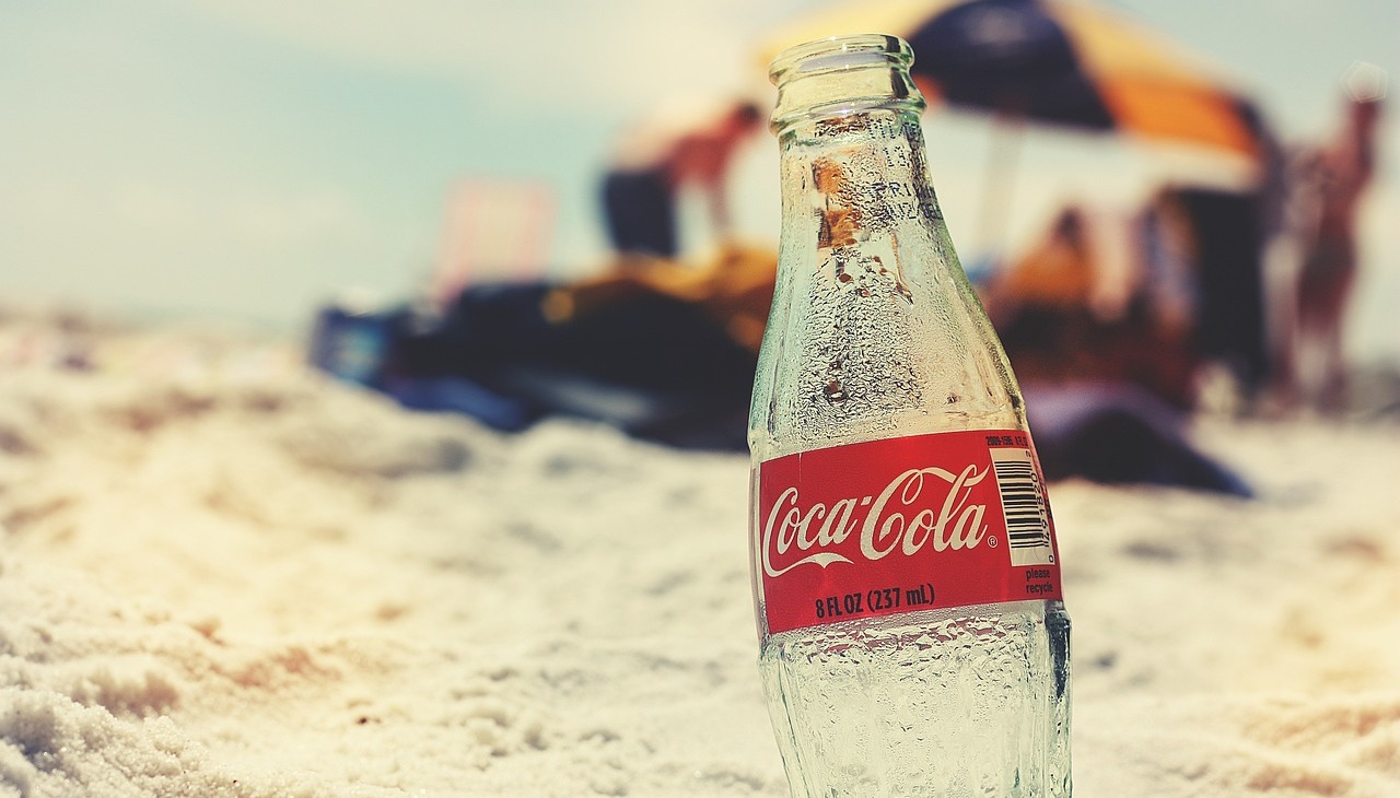 An almost empty bottle of coke on a beach.