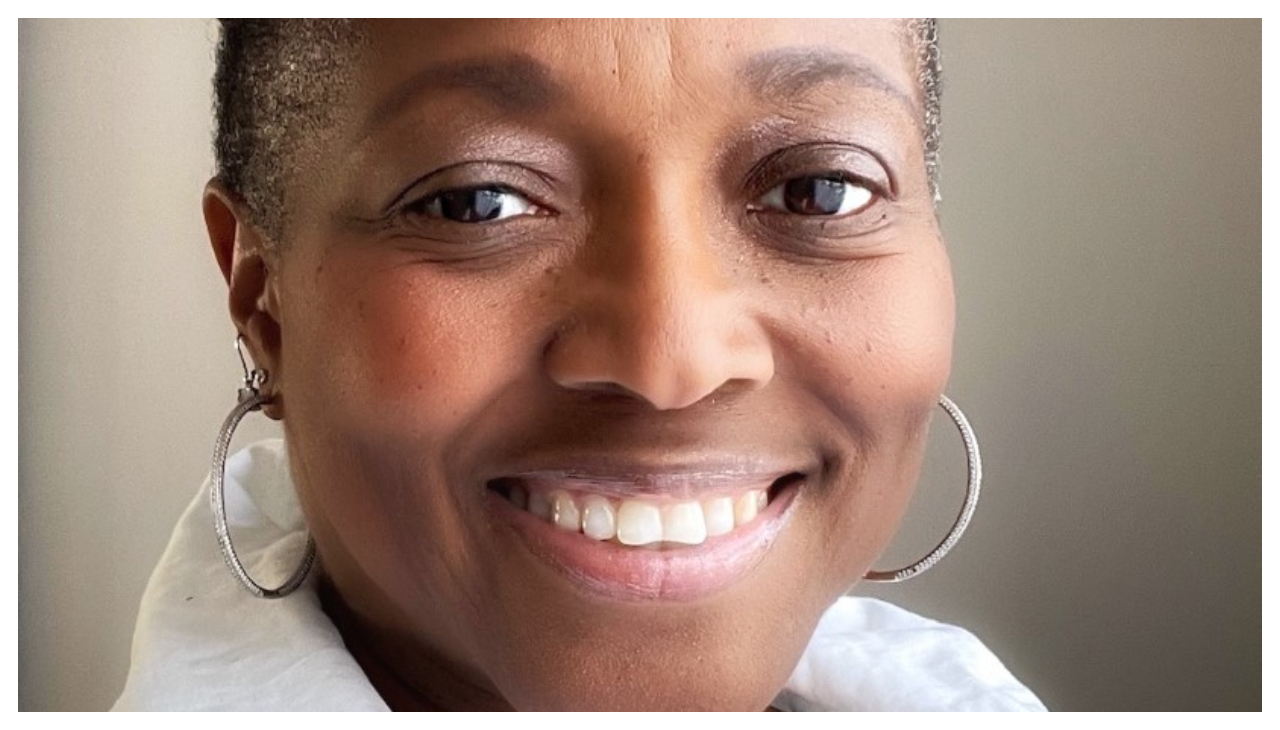 Rev. Dr. Karen Georgia Thompson, a Jamaican woman wearing a white sweater and with two thin hoop earrings. She has short hair, is facing the viewer, and is smiling.