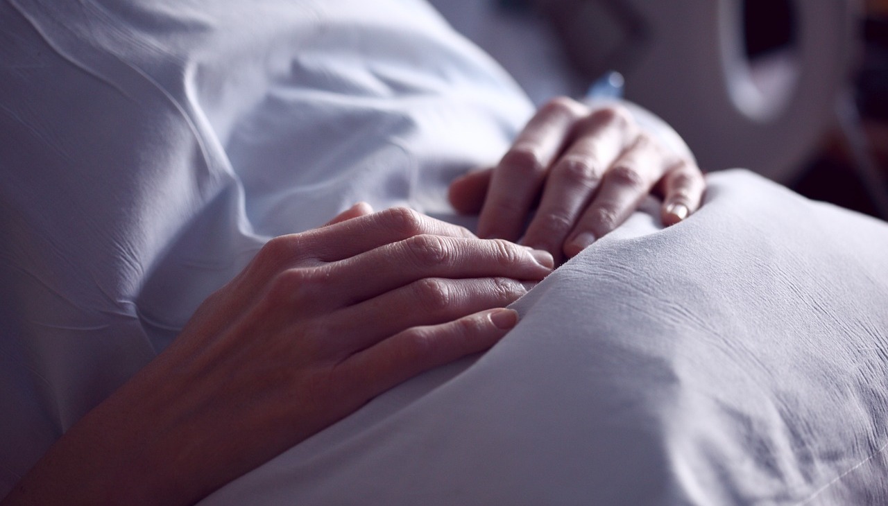 A patient lies on bed with his hands above his belly. 