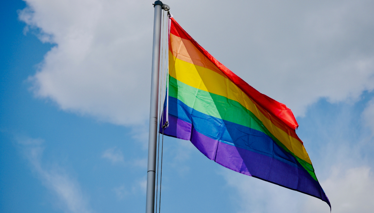 Pride flag on a flagpole. Photo by Sophie Emeny on Unsplash