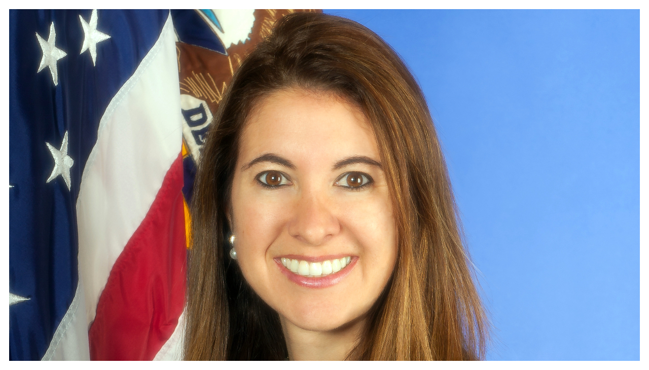 Adriana Kugler, a woman with long brown hair, shown from the neck up. She is facing the viewer and is smiling.