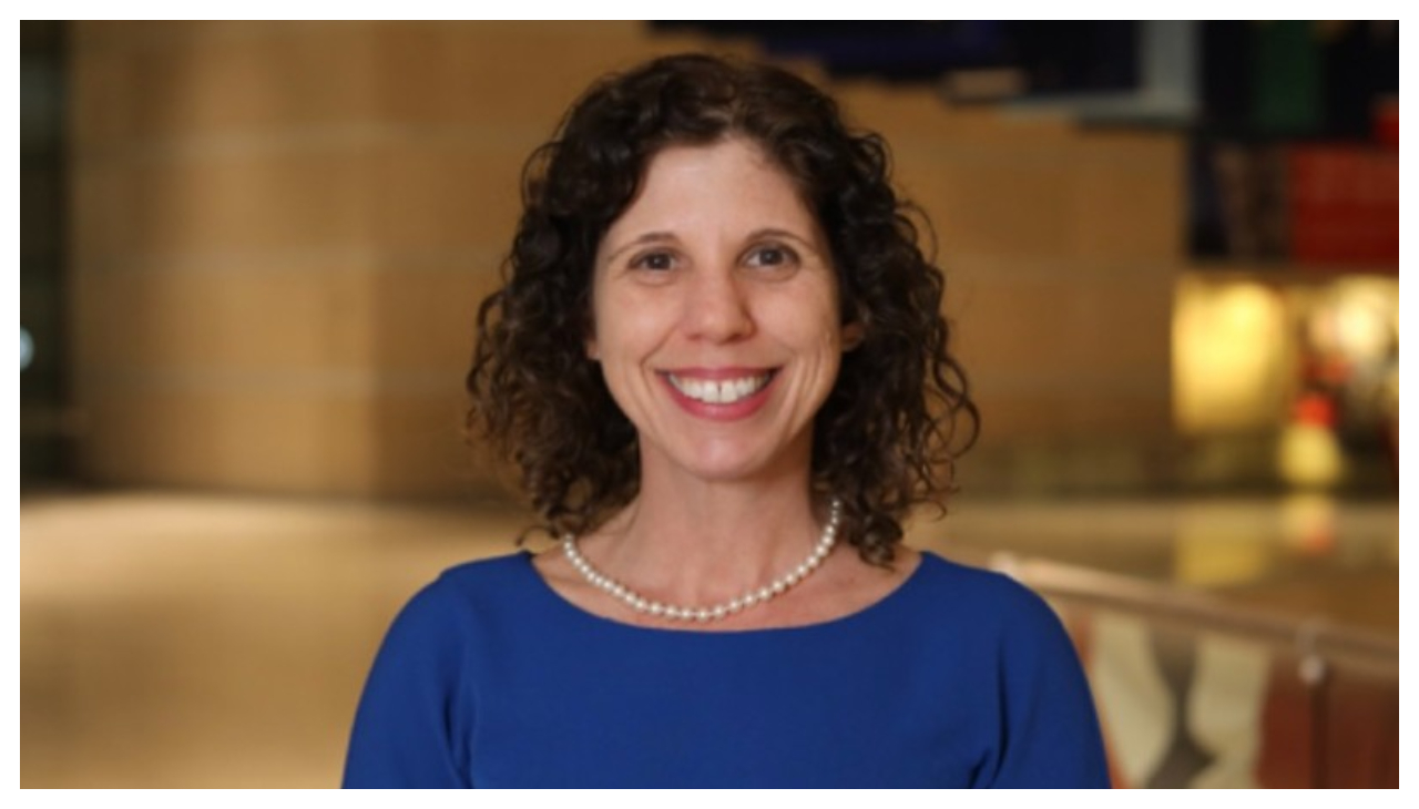 Kerry Sautner, a light skinned woman with short curly hair. She is facing the viewer and is smiling.