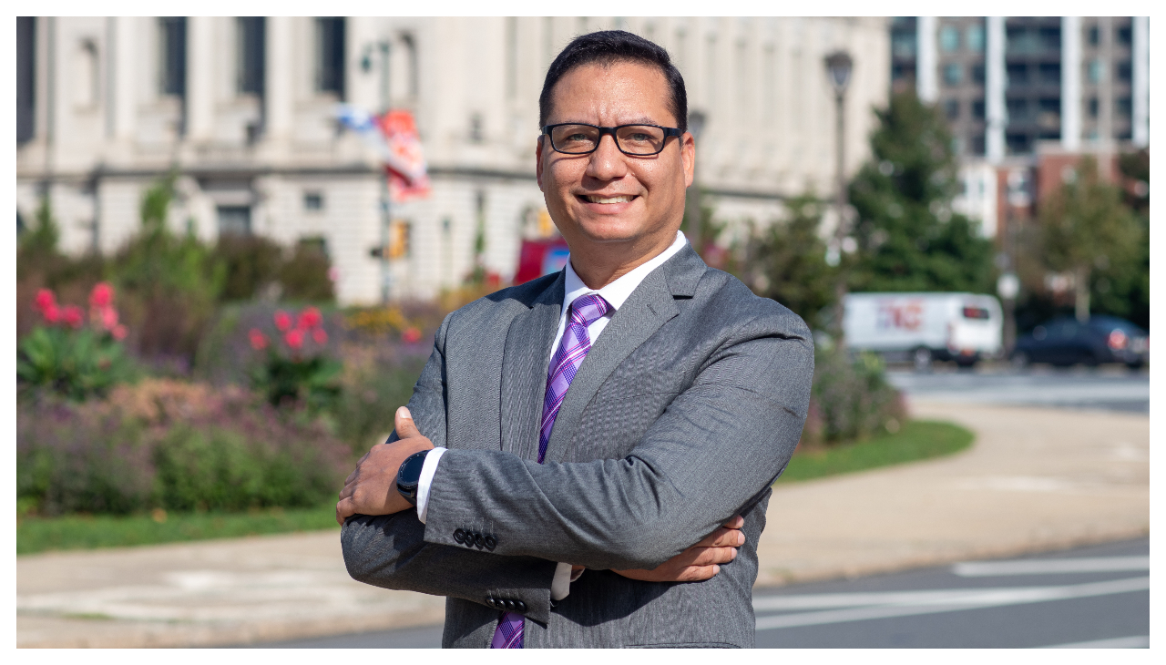 Orlando Rendon, a latino man in a gray business suit. He is standing with his arms crossed and is facing the viewer.