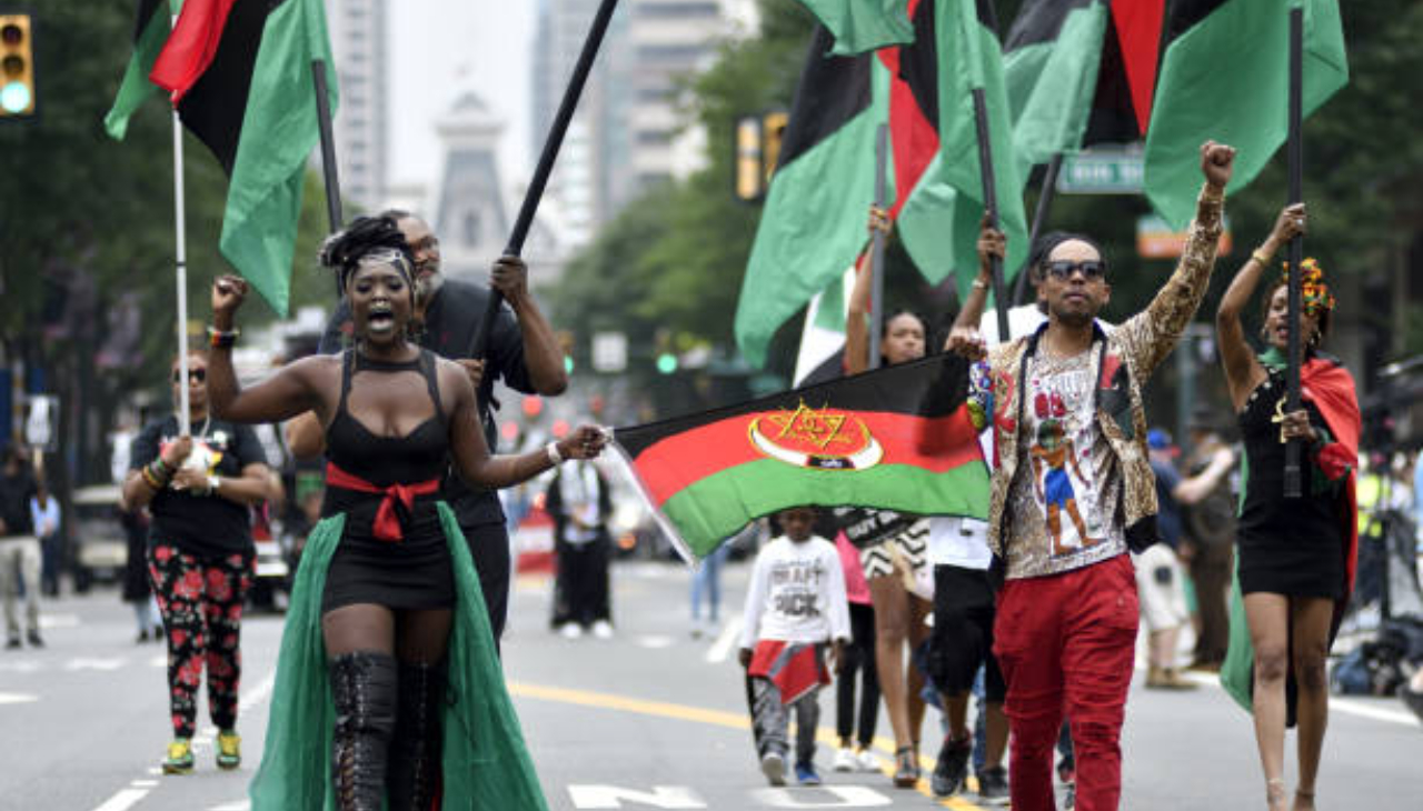 A group of several people holding flags of the RBG brigade marching down Market Street in Philadelphia.