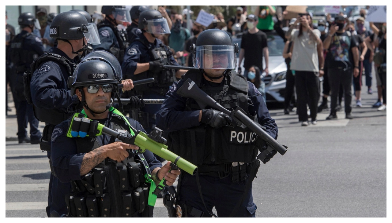 Several armed police officers in body armor standing before a crowd of protestors.