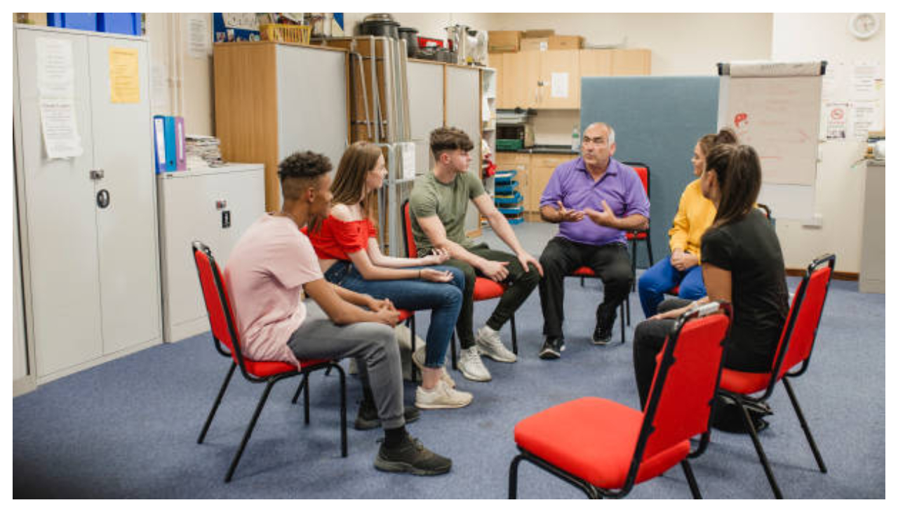 A group of teenagers sitting in chairs in a circle discussing with one another.