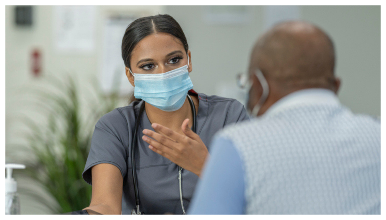 A Latina physician speaking to a Black patient in a medical office.