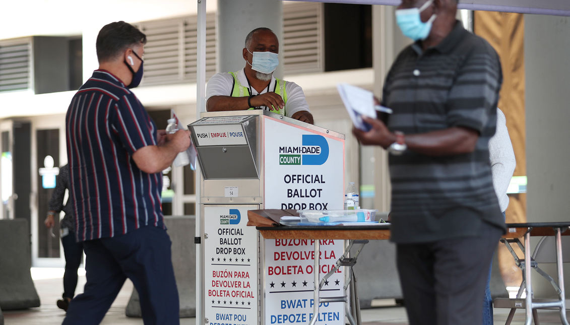 Poll workers help a voter put their mail-in ballot in an official Miami-Dade County ballot drop box on August 11, 2020 in Miami, Florida. (Photo by Joe Raedle/Getty Images)