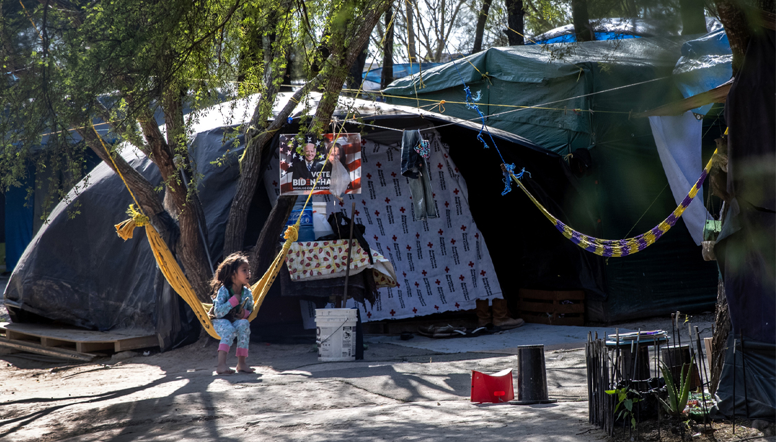 A Salvadorian girl sits near a Biden-Harris campaign poster inside a camp for asylum seekers on February 07, 2021 in Matamoros, Mexico. Many of the some 600 people in the camp, most from Central America, have been living there for up to a year, waiting for an immigration court hearing across the bridge in Brownsville, Texas. (Photo by John Moore/Getty Images)
