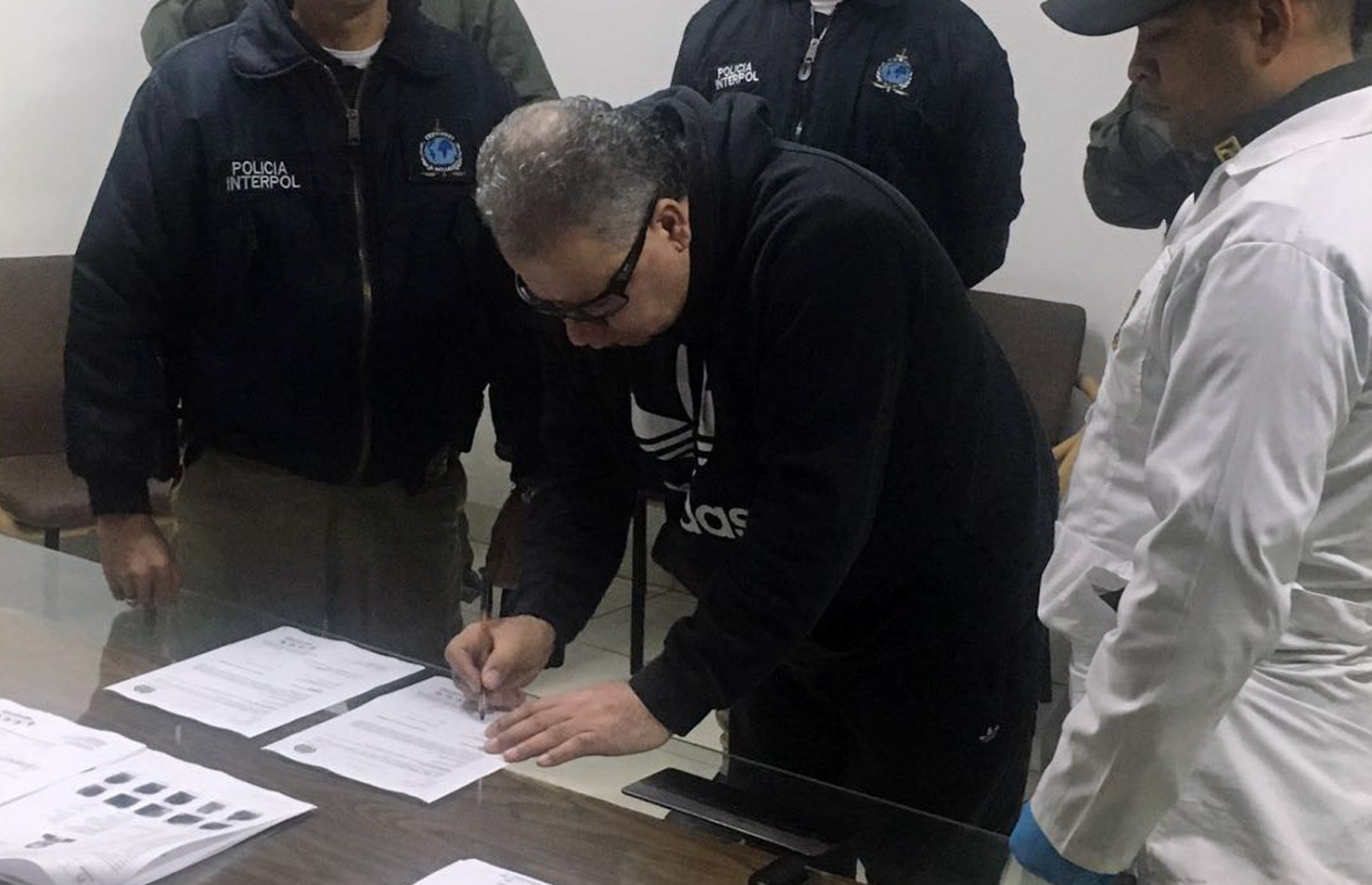 Former militia commander Daniel Rendon Herrera (C) signs documents as Interpol agents watch on April 23, 2018, in Bogota, Colombia. EPA-EFE/Colombian National Police
