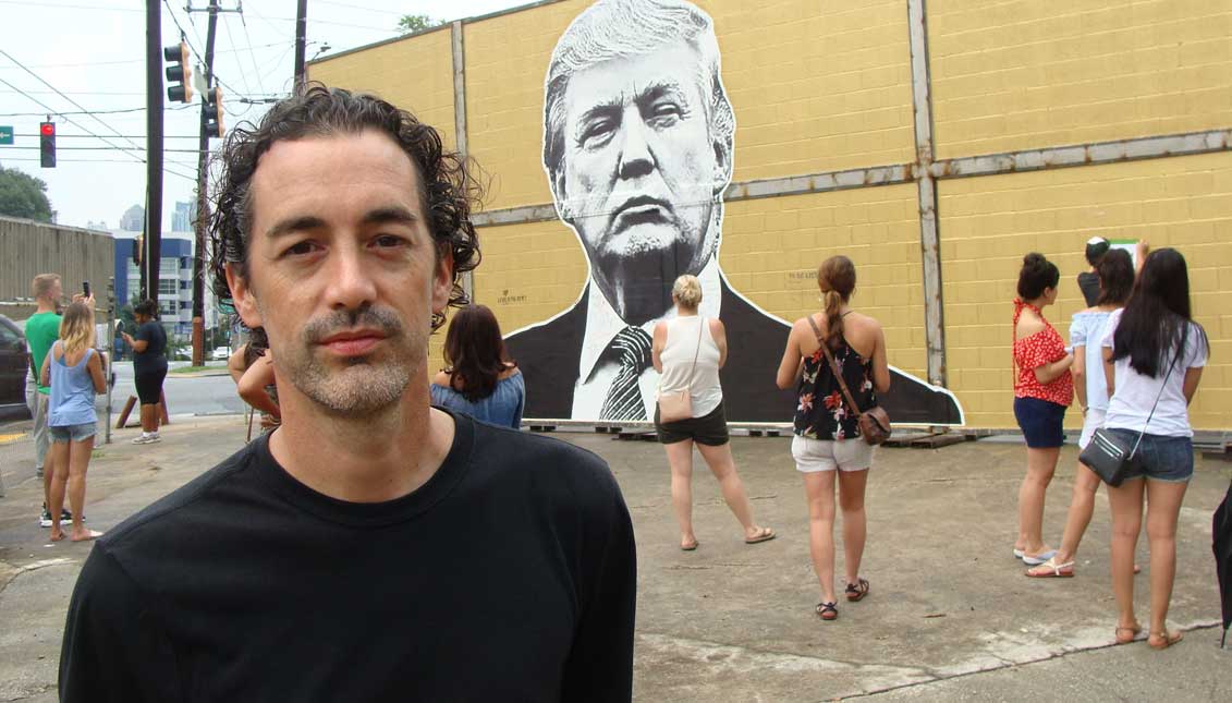 The American artist Joseph Guay poses next to a wall that he designed to raise awareness about migratory problems.
