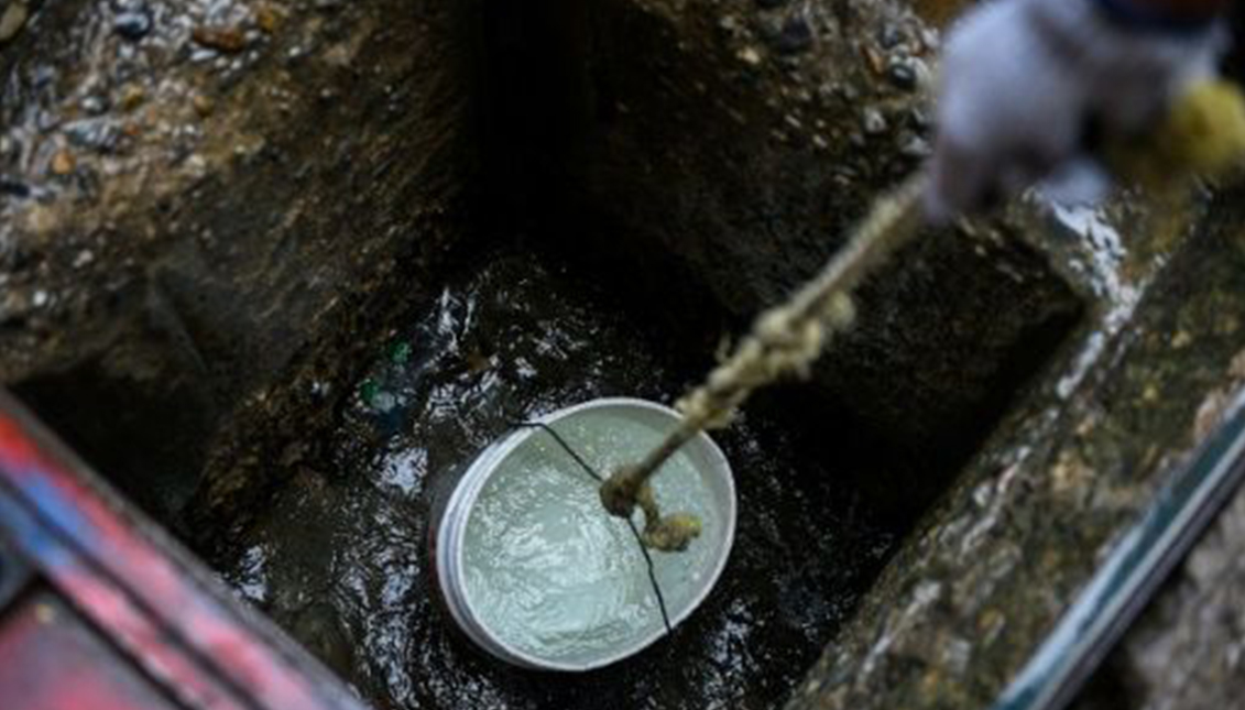 Personas sacan agua de un pozo para usarla en sus baños, en la barriada caraqueña de Petare, el 1 de abril de 2019. Photo: AFP / Federico Parra-