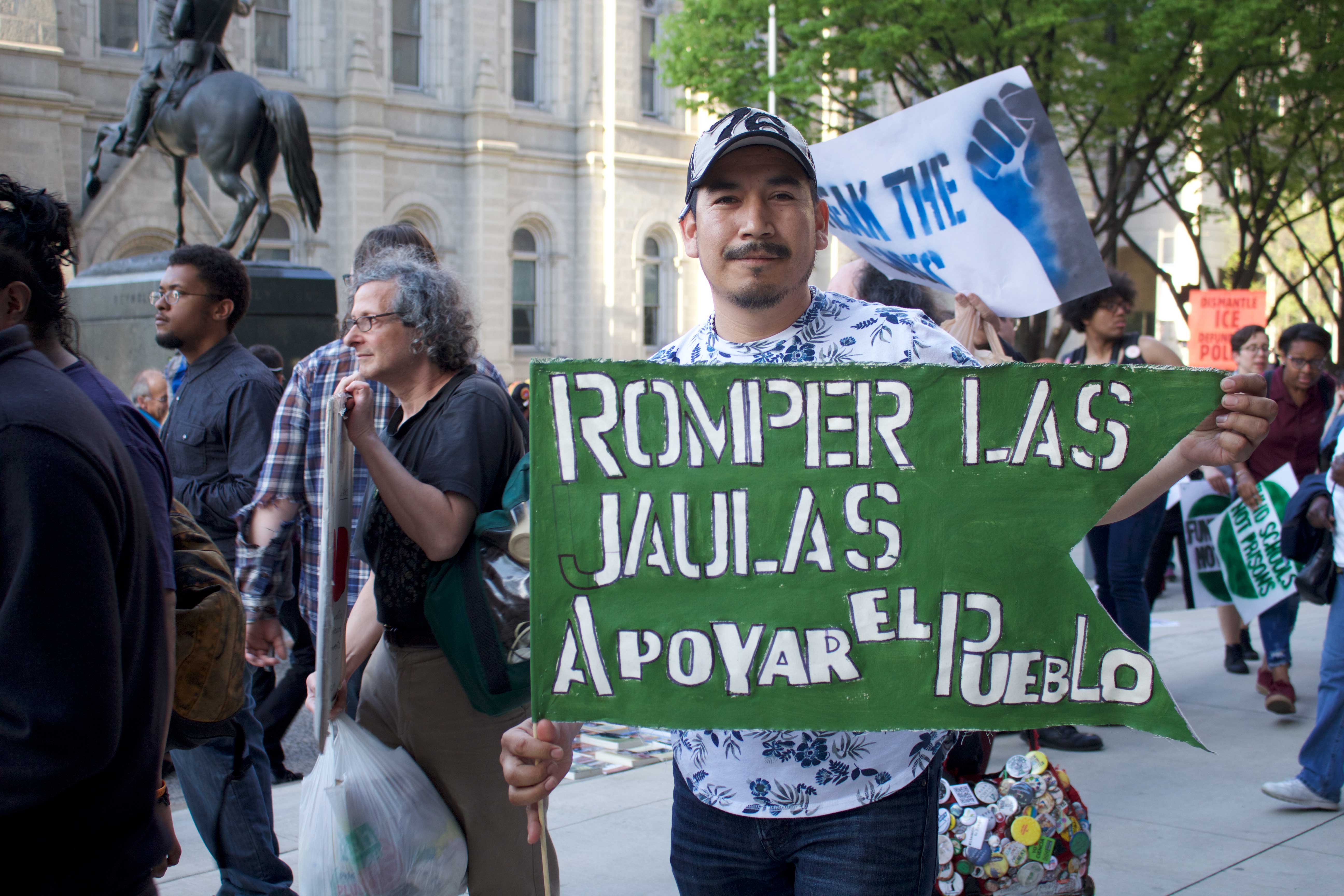 A man poses with a sign that translates to "Break the cages, support the people" at the Break the Cages, Fund the People May Day rally at Philadelphia City Hall. Photo: Emily Neil / AL DÍA News