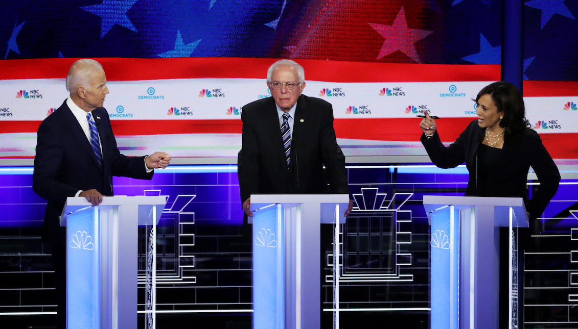 MIAMI, FLORIDA - JUNE 27: Sen. Kamala Harris (R) (D-CA) and former Vice President Joe Biden (L) speak as Sen. Bernie Sanders (I-VT) looks on during the second night of the first Democratic presidential debate on June 27, 2019 in Miami, Florida. (Photo by Drew Angerer/Getty Images)