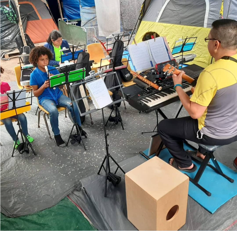 Ernesto Hernandez teaching music lessons to children at Camp Matamoros. Image courtesy of Instagram @ernestohnz.