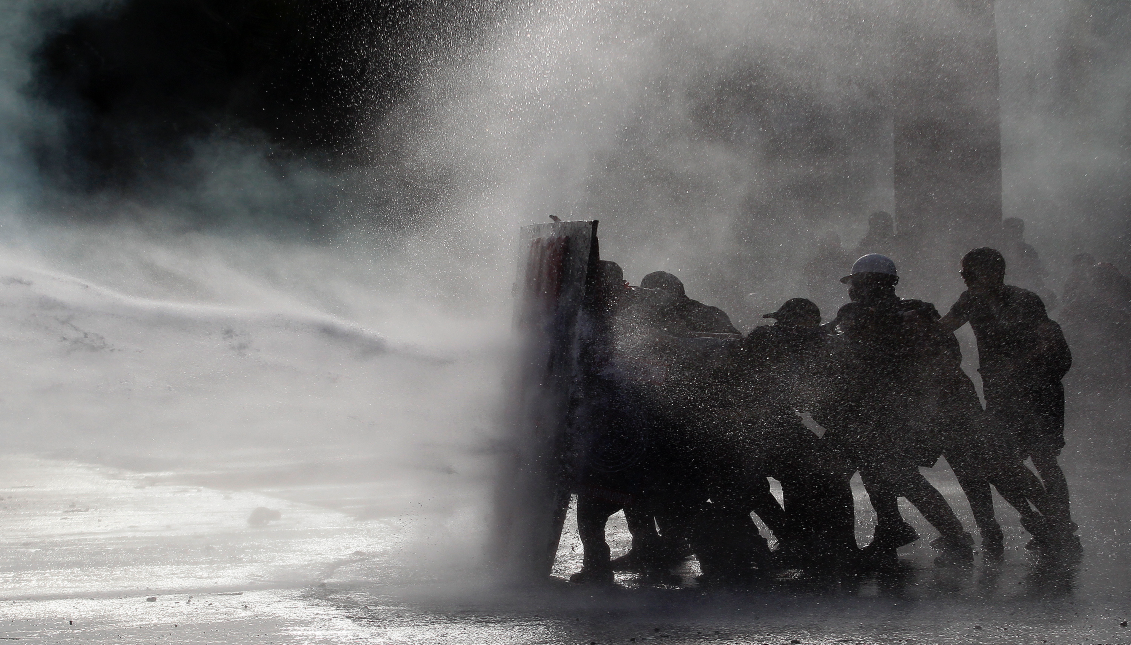 SANTIAGO, CHILE - NOVEMBER 28: Demonstrators protect themselves from water during a protest against government of President Sebastian Piñera at Plaza Italia on November 28, 2019 in Santiago, Chile.  (Photo by Marcelo Hernandez/Getty Images)