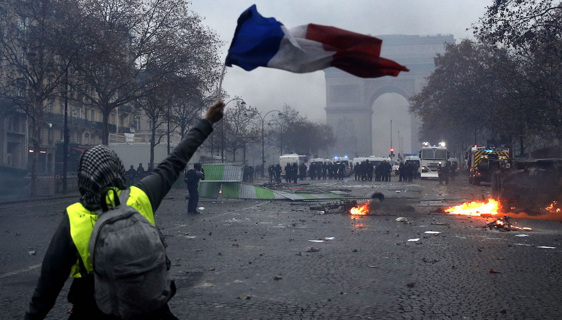 A protester wearing a yellow vest (gilets jaunes) waves a French flag during clashes with riot police near the Arc de Triomphe as part of a demonstration on high fuel prices on the Champs-Elysees in Paris, France, on May 1. December 2018. EFE/EPA/YOAN VALAT