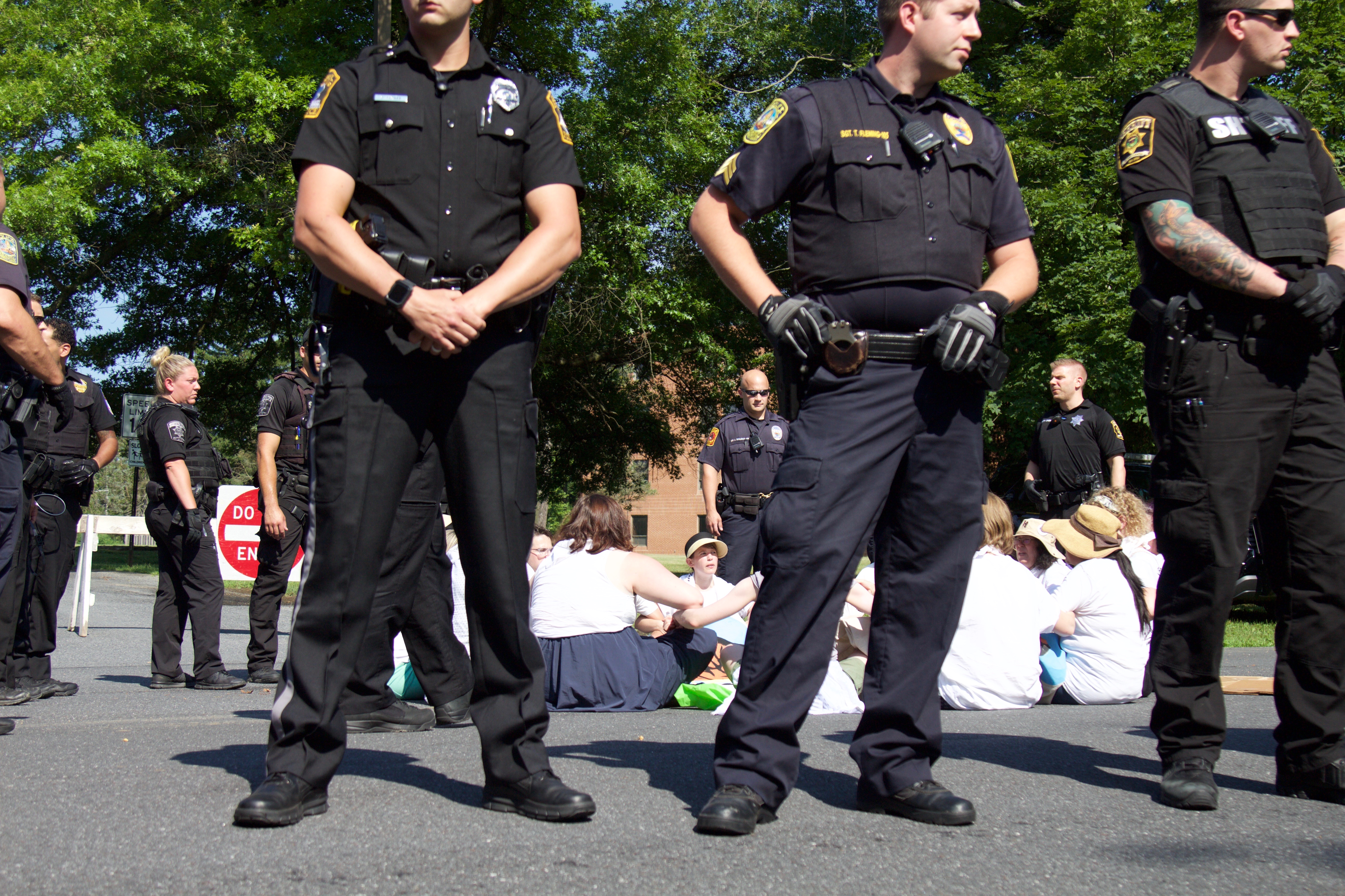 Police officers surround nearly 20 demonstrators from the Shut Down Berks Coalition, who linked arms and sat down in the road to block the entrance to the Berks County Residential Center as part of their call for Governor Tom Wolf to shut down the facility, which currently detains about 20 immigrant families. Photo: Emily Neil / AL DÍA News
