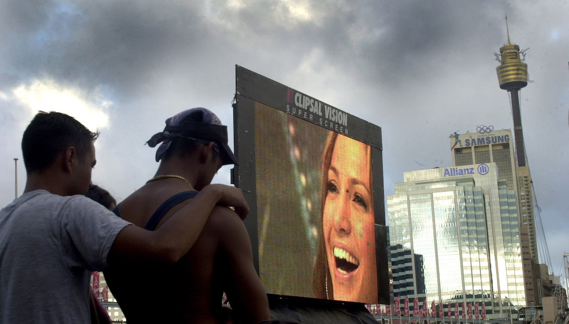 Two men watch as singer Jennifer Lopez's performance is projected on a video screen on February 22, 2001, in Sydney, Australia. (Photo by Jeremy Piper/Newsmakers)