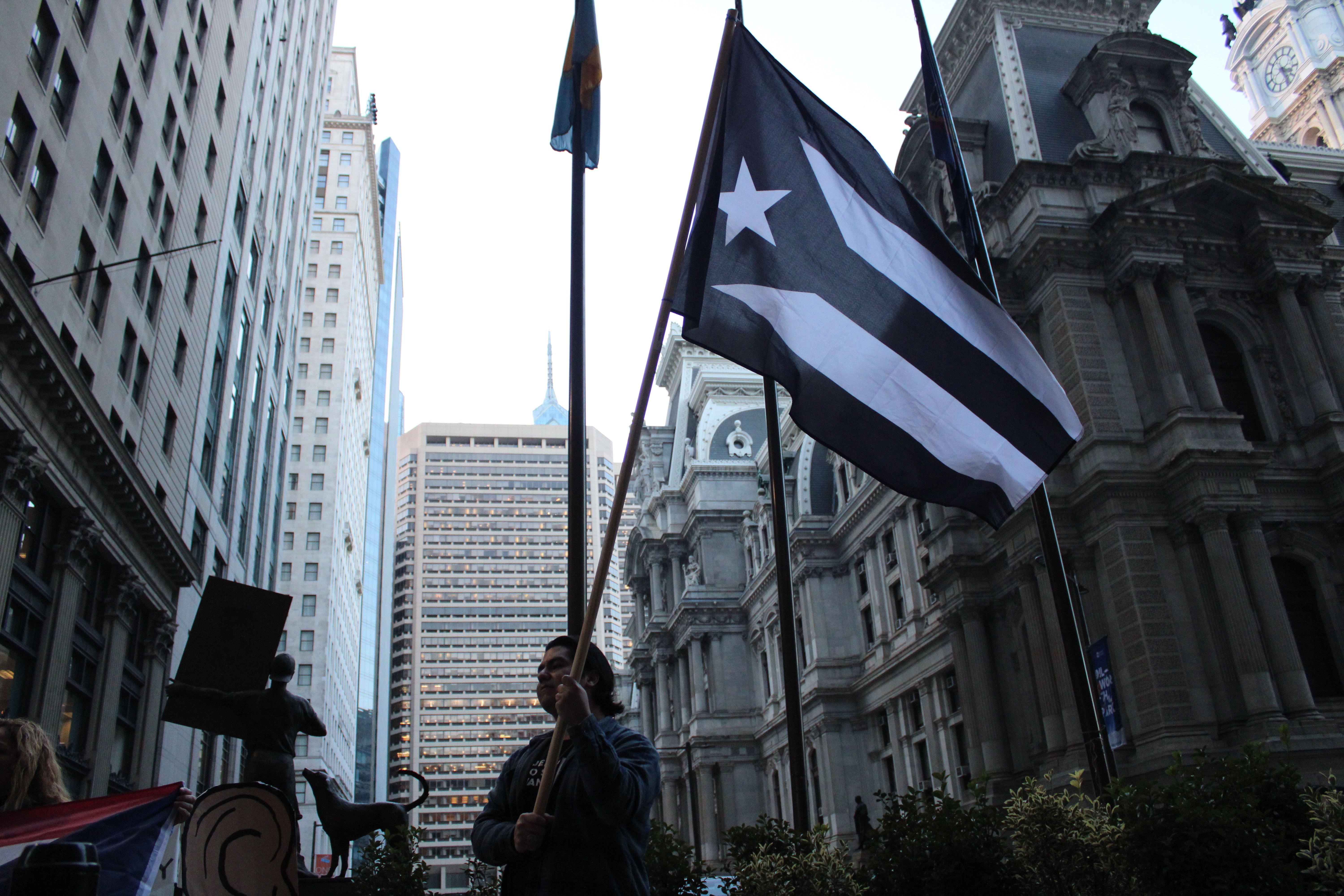 Adrian Mercado of Philly Boricuas lifts the Puerto Rican independence flag, as protesters gathered outside of the Department of Urban Housing and Development offices in Center City, Philadelphia, demanding that HUD release the more than $10 billion in aid allocated to Puerto Rico after Hurricanes María and Irma. Photo: Emily Neil / AL DÍA News