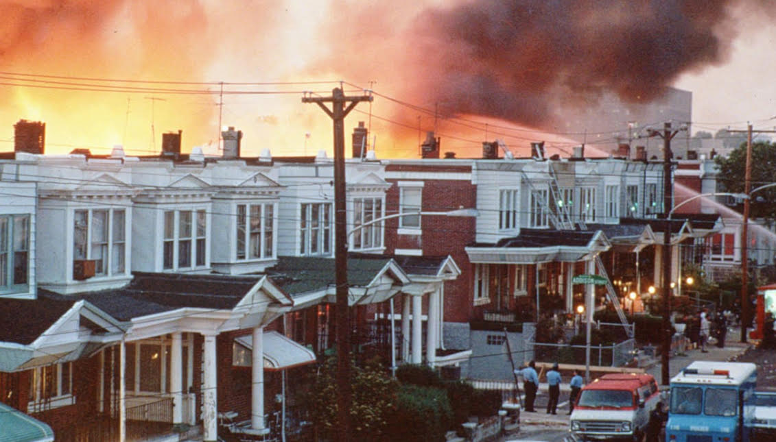 Apologies were finally issued by the city for its role in the MOVE Bombing of 1985.Row houses in Philadelphia burn after policed dropped a bomb on the Move house in May 1985. Photograph: AP