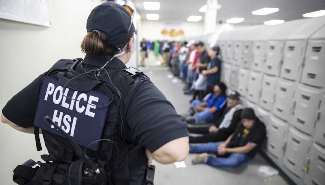 A US Immigration and Customs Enforcement officer walks past detained immigrants during a raid at a Mississippi chicken processing plant. US Department of Homeland Security/Immigration and Customs Enforcement.